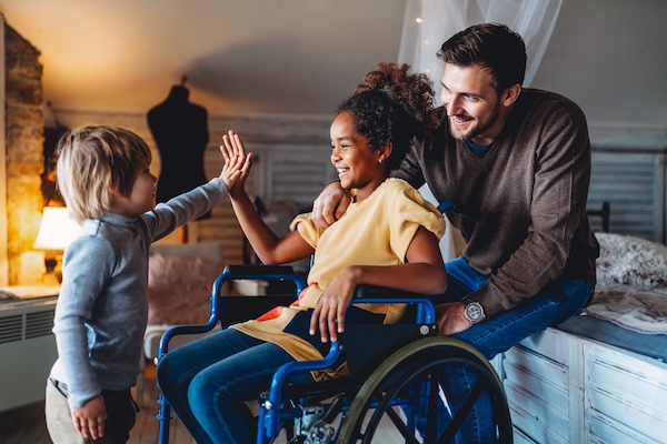 Happy multiethnic loving family. Smiling little girl with disability in wheelchair at home