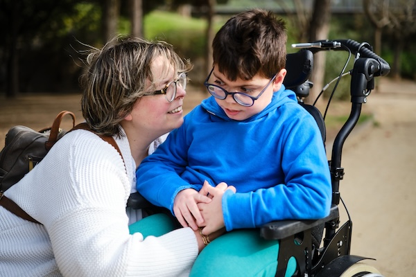 Disabled boy in a wheelchair enjoying a walk outdoors with his mother. Disability concept.